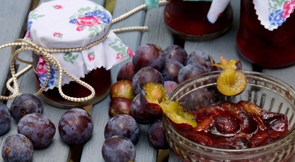 Un bol cu dulceață de prune, prune întregi și borcane de gem pe o masă de lemn