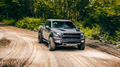 Care este diferenţa dintre anvelopele XL şi cele obişnuite - Care este diferenţa dintre anvelopele XL şi cele obişnuite – O mașină neagră, Ford Raptor, circulă pe un drum off-road de pământ plin de praf, cu o pădure verde densă în fundal