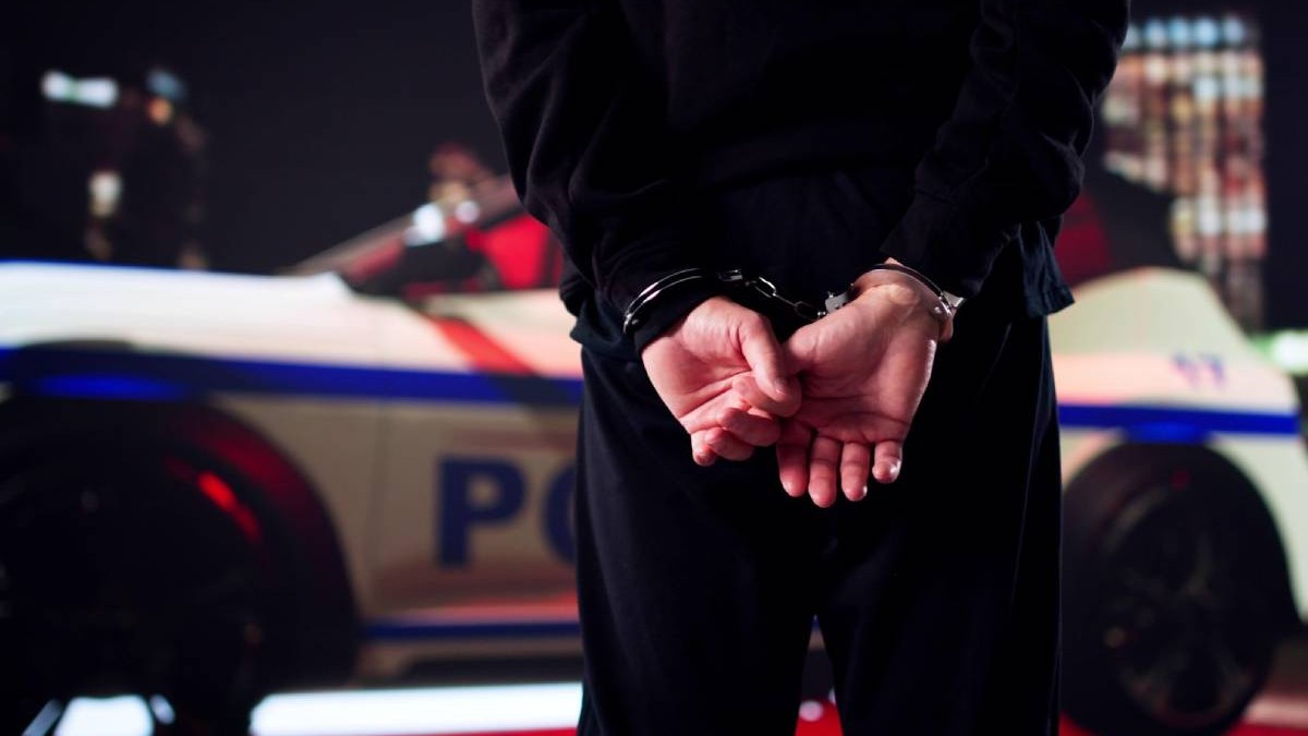 Imagine de noapte, in prim plan o persoana in haine negre, cu catuse la maine, in fundal se vede , neclara, o masina de politie