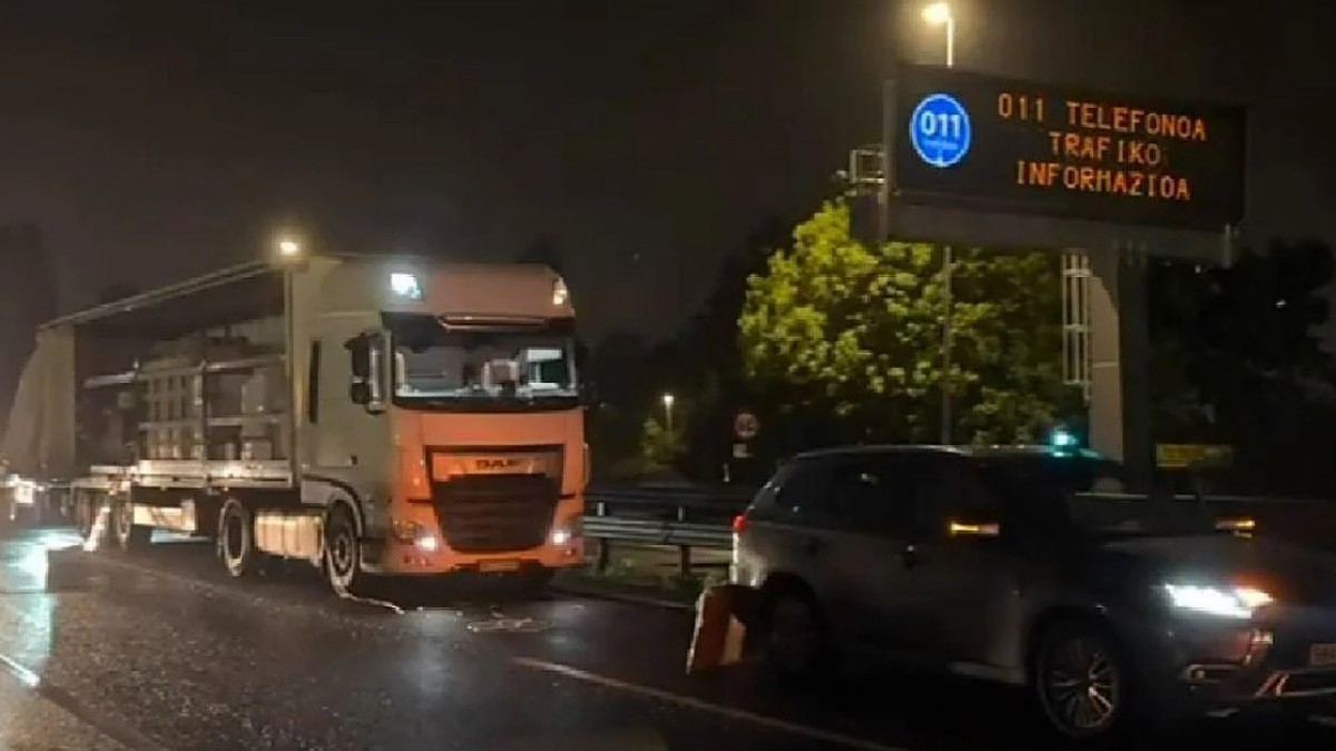 Un camion alb oprit noaptea pe marginea unui drum, alături de un alt autoturism, în apropierea unui panou electronic de informare rutieră.
