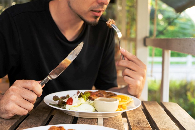 Guy eating steak at a table in a summer cafe.