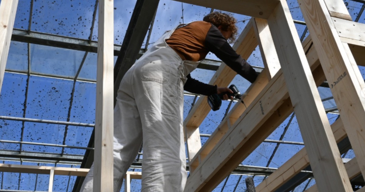 O femeie în salopetă care se află în interiorul unei structuri de lemn.