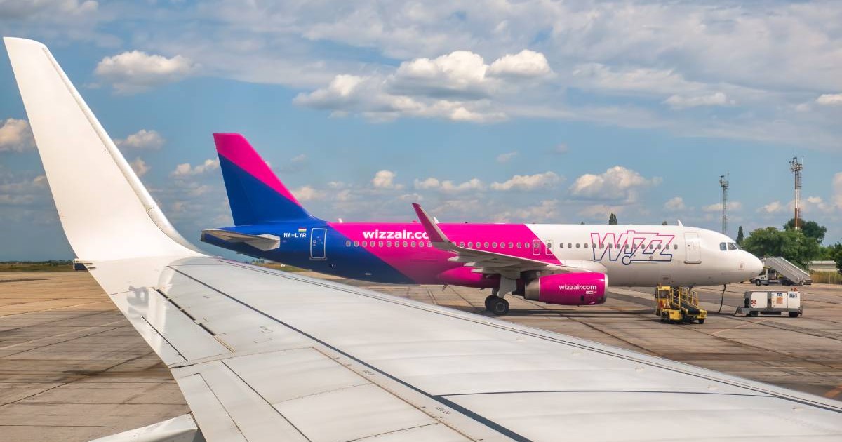 Un avion Wizz Air, colorat cu roz și albastru, stând pe pistă, în timp ce pilotul așteaptă să decoleze