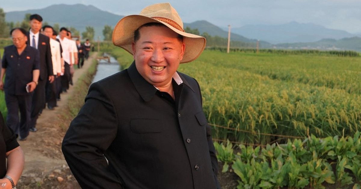 fotografie, făcută pe 24 iulie 2025, îl prezintă pe liderul nord-coreean Kim Jong-un, in costum negru, palarie de paie pe cap si mainile in buzunare, inspectarea unei baze de aprovizionare a unei unități a Armatei Populare Coreene, in mijlocul unui camp, mai multi lucratori in spatele lui