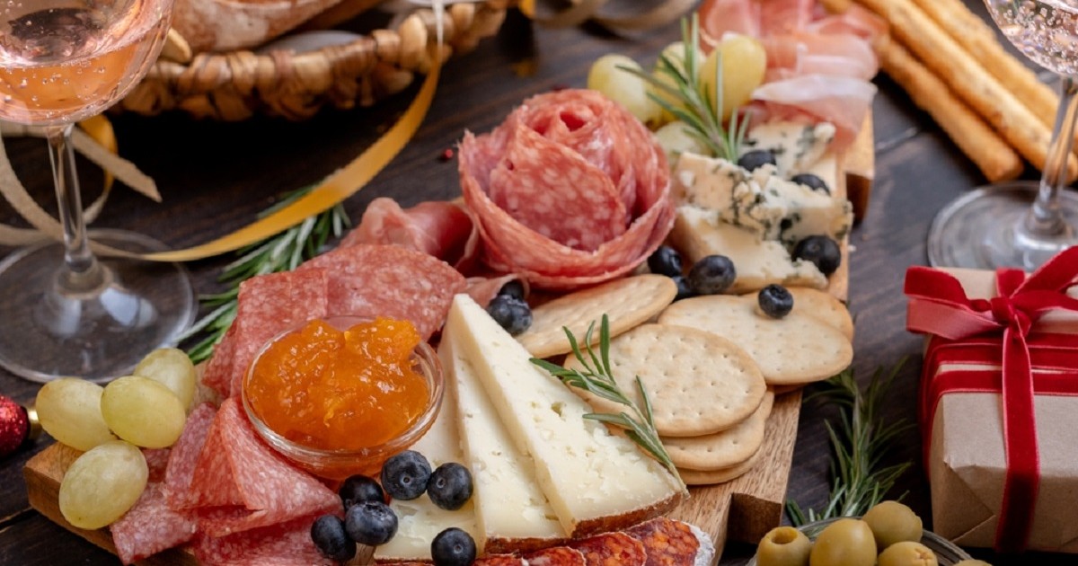 Brunch-ul perfect acasă: cum să faci un platou spectaculos pentru musafiri - un platou cu mezeluri si branzeturi cu frunze de rozmarin, asezat pe o masa festiva alaturi de cateva pahare de vin
