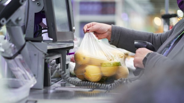 O casieră care scanează o pungă din plastic plină cu lămâi la casa de marcat a unui magazin sau supermarket.   