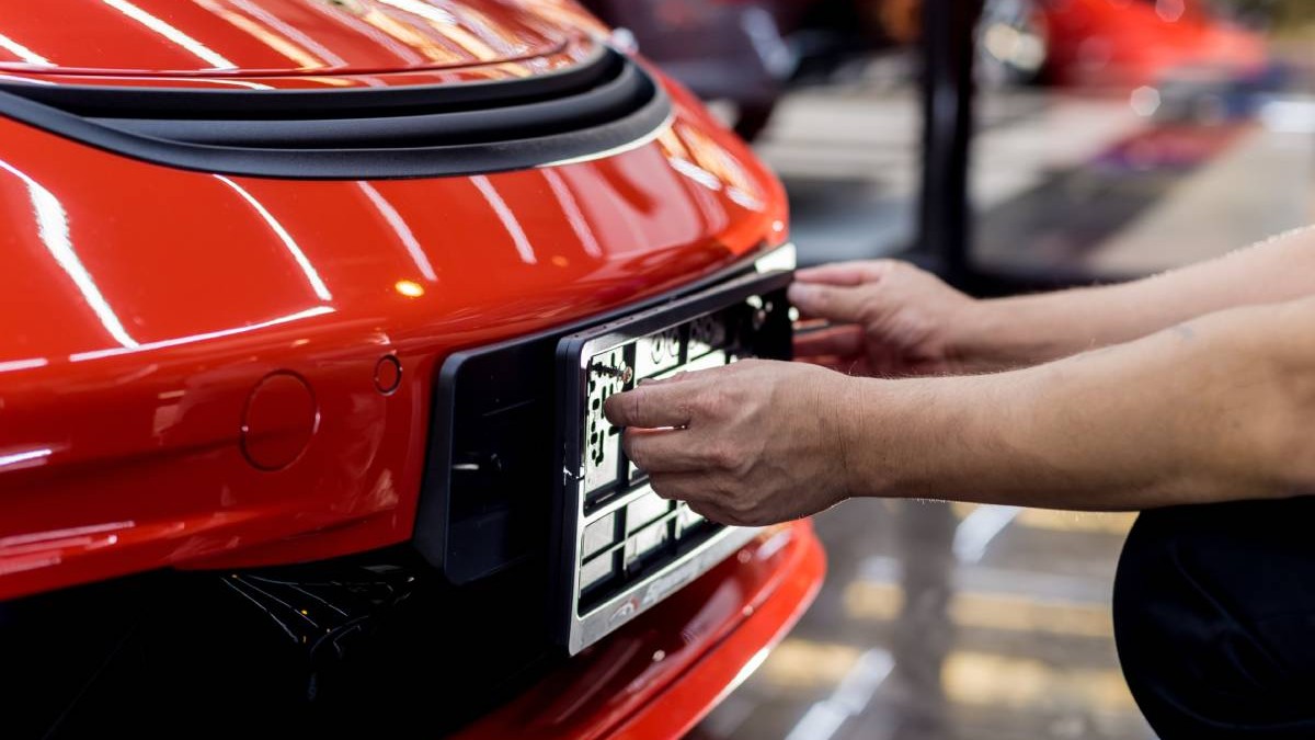 O persoană montează suportul de număr auto pe o mașină roșie.