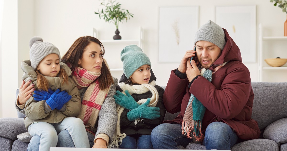 O familie stă pe canapea îmbrăcată gros, cu căciuli, mănuși și fulare, semn că în locuință este foarte frig. În fața lor se află un calorifer, iar bărbatul vorbește la telefon, sugerând o încercare disperată de a rezolva problema încălzirii.