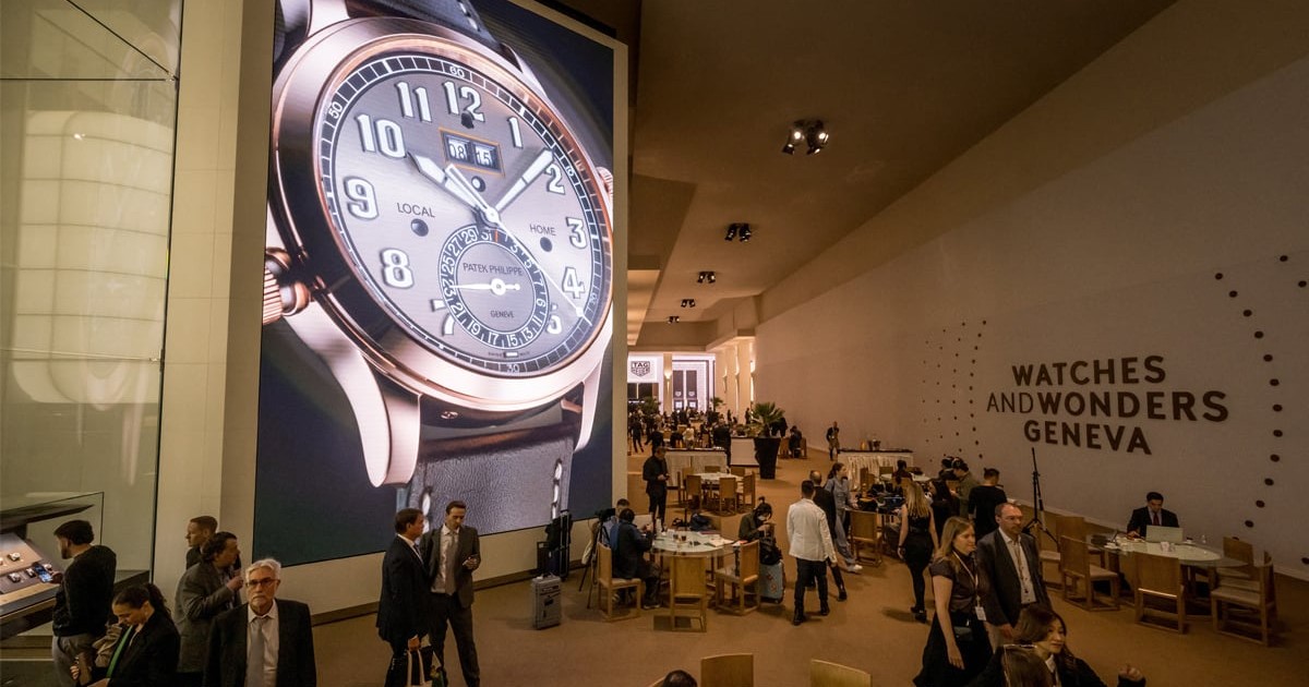 Un afiș cu un ceas mare expus pe lîngă care trec oamenii careu au venit la Watches and Wonders din Geneva.