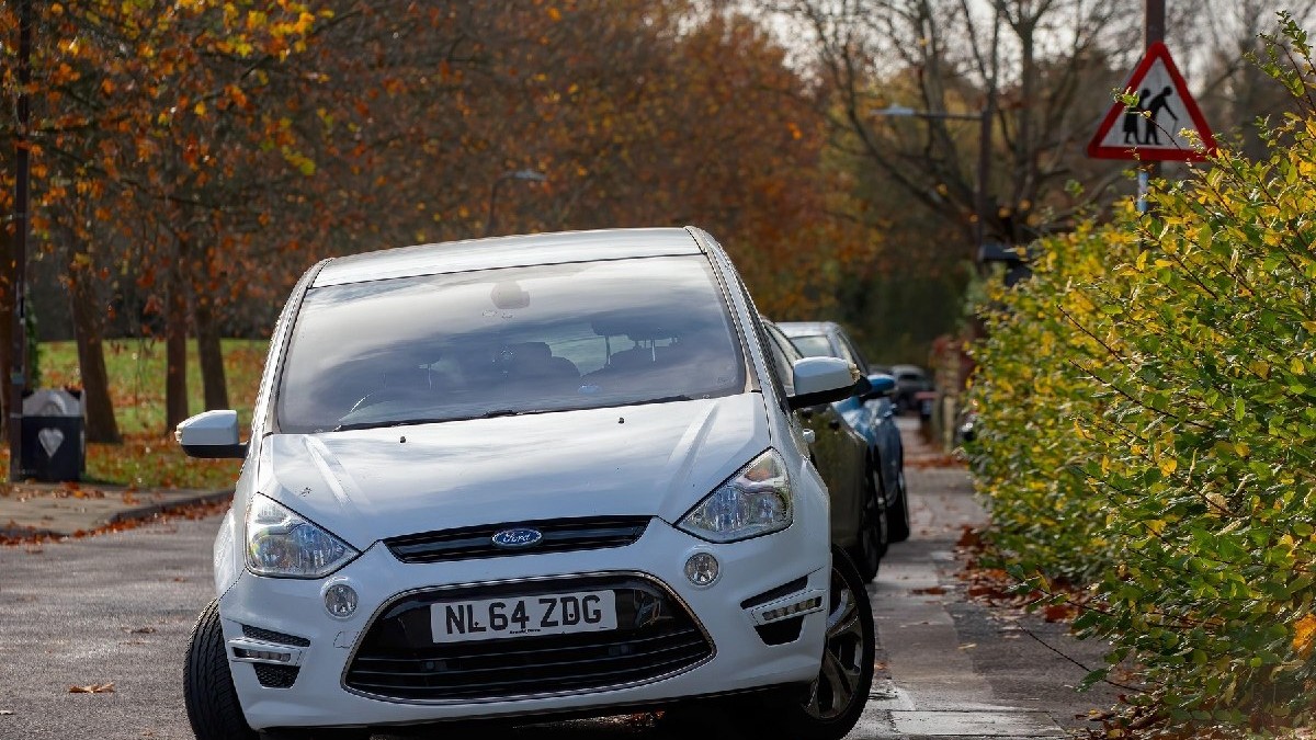 Milton Keynes, Bucks, Marea Britanie - 8 noiembrie 2025: Șir de mașini parcate pe trotuar lângă un indicator rutier care avertizează asupra prezenței pietonilor fragili și vârstnici.
