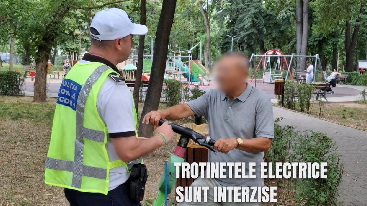 Un politist local il amendeaza pe un bărbat care circula pe o trotineta electriva verde intr-un parc