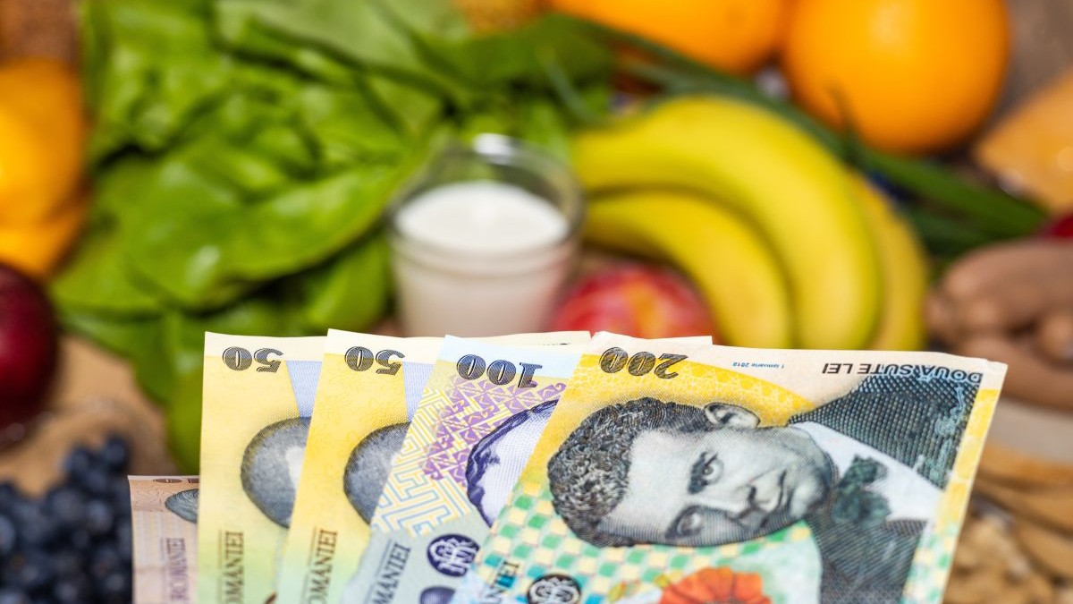 Bancnote de lei românești, de 200, 100 și 50 de lei, peste un raft cu fructe, într-un supermarket