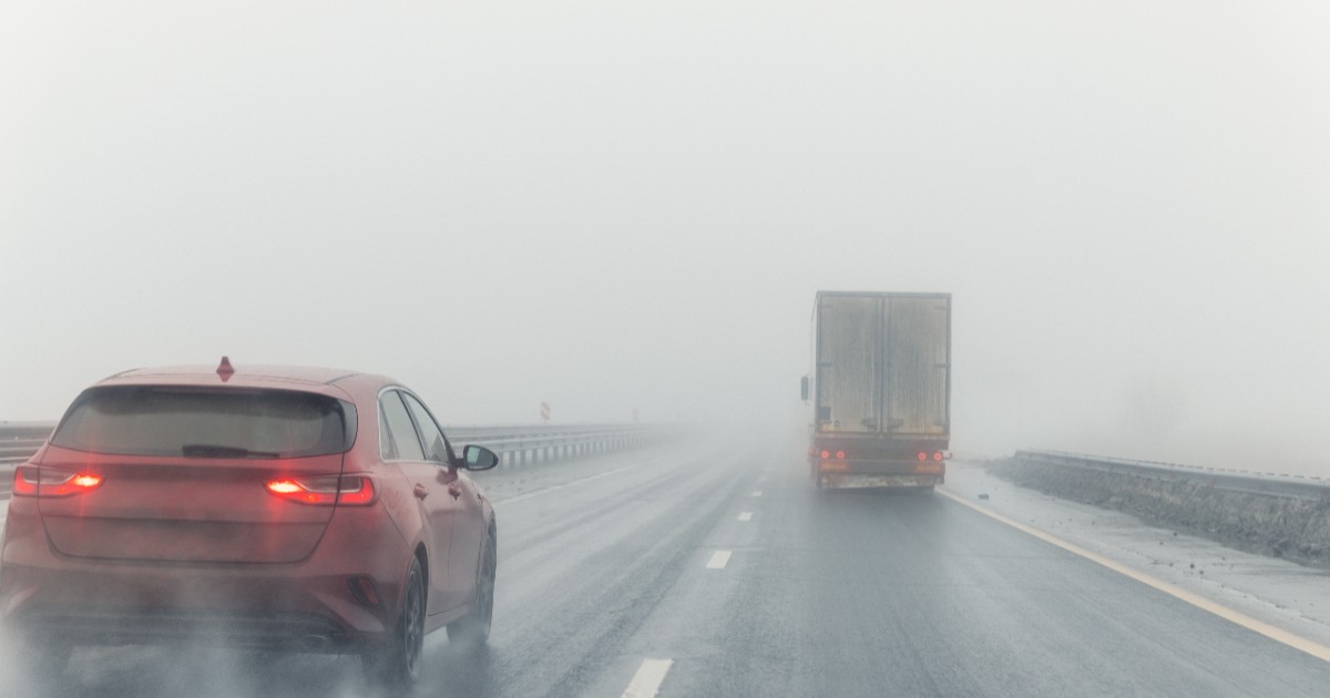 O mașină roșie și un TIR care circulă pe șosea, pe ceață