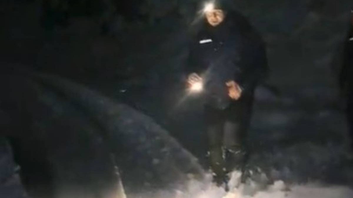 Un salvator in uniforma, cu o lanterna pe cap si una in mana, noaptea, in viscol si zapada