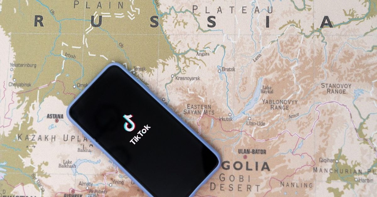 Sigla TikTok pe ecranul smartphone-ului pe fundalul hărții Rusiei. Conceptul de influenta a Rusiei pe social media