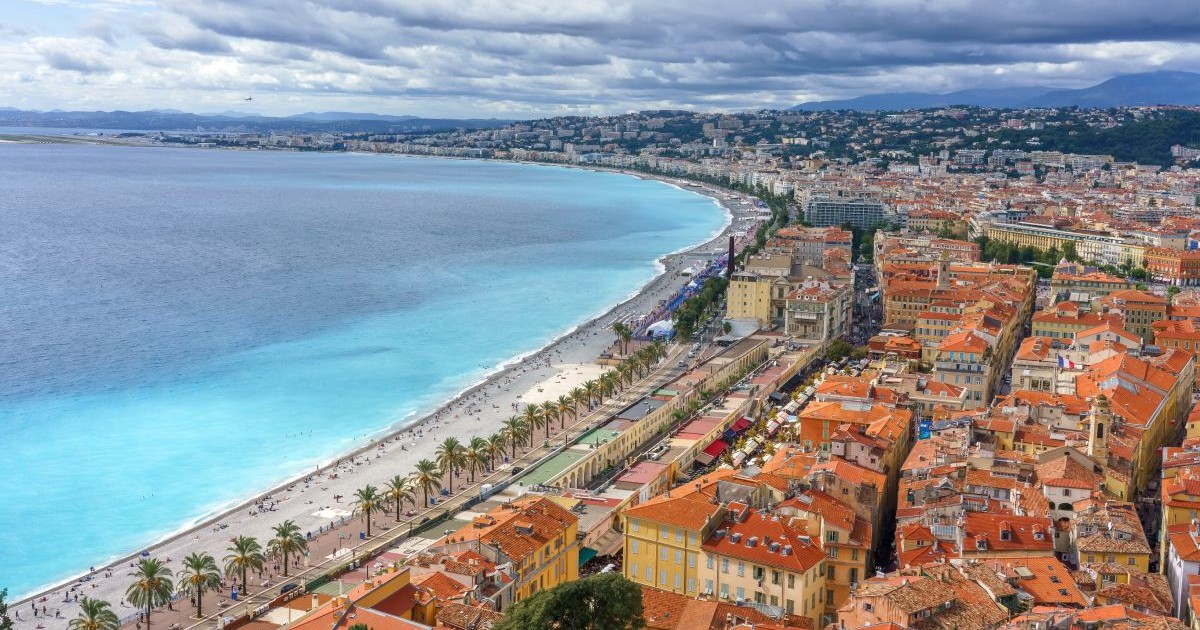 Imagine aeriană cu promenada orașului Nisa, din Franța, pe Coasta de Azur, cu jumătatea dreaptă în care se văd casele cu acoperișuri portocalii și în stânga marea turcoaz