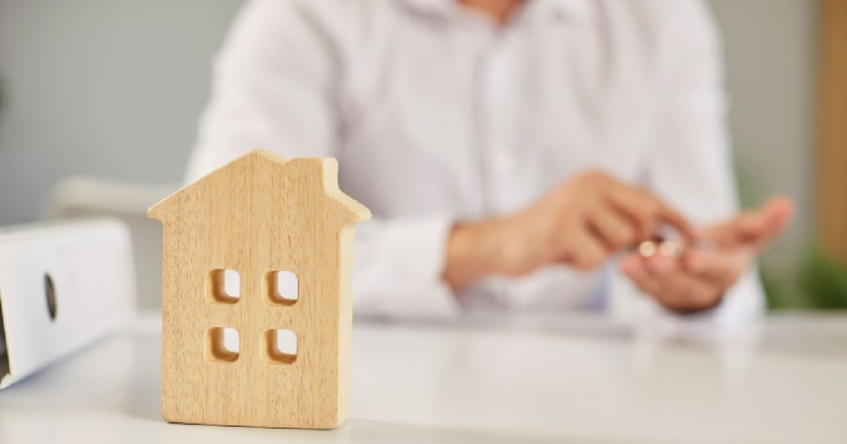 O figurină reprezentând o casă din lemn așezată pe un birou, cu un agent imobiliar care lucrează în birou.