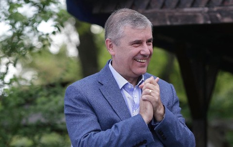 Lucian Pahonțu în costum bleumarin cu mâinile împreunate, râzând