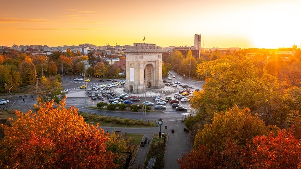 Fotografie aeriană care înfățișează Arcul de Triumf, un monument istoric din București, în timpul unui frumos apus de toamnă. 