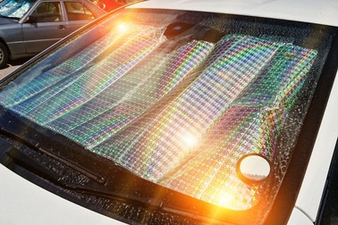 Windshield of car with protective reflective sunscreen surface inside car parked on street with sunbeams. Method for protecting heated by sun rays car