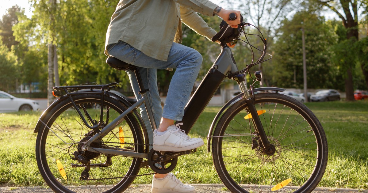 Un tânăr, pe o bicicletă electrică, plimbându-se într-un parc.