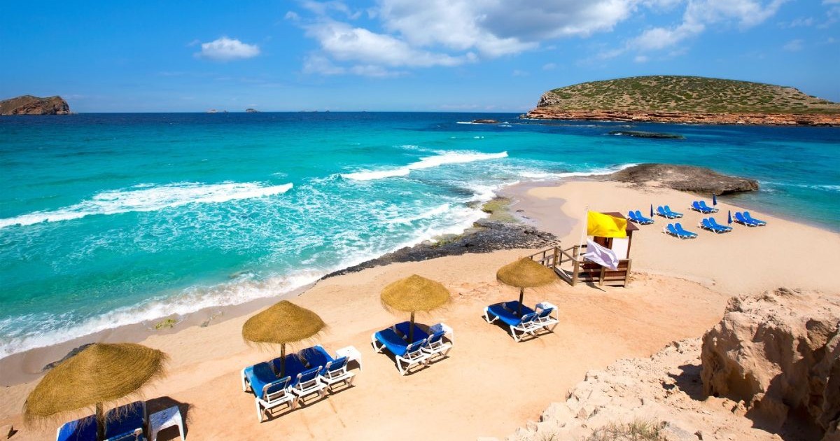 Plaja Cala Conte de pe insula Ibiza, cu șezlonguri și umbrele, iar apa mării de culoare albastru deschis