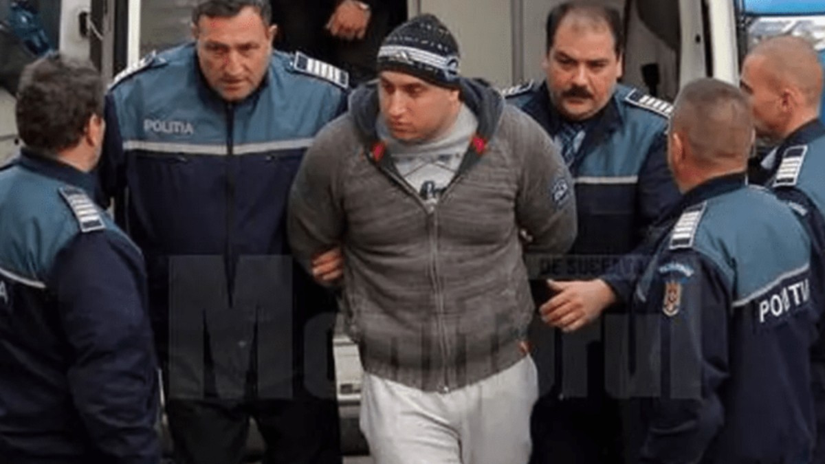 Alexandru Huțuleac este escortat de mai mulți polițiști. Acesta poartă un hanorac gri, pantaloni sport albi și o căciulă