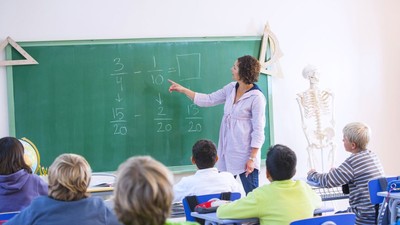 Teacher at front of class, explaining maths problem on blackboard