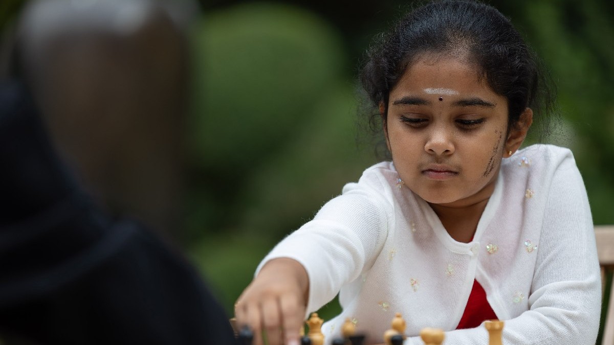 Bodhana Sivanandan, campioana la șah din Marea Britanie, îmbrăcată cu bluză roșie și bolero alb, în fața unei table de șah 28 august 2023