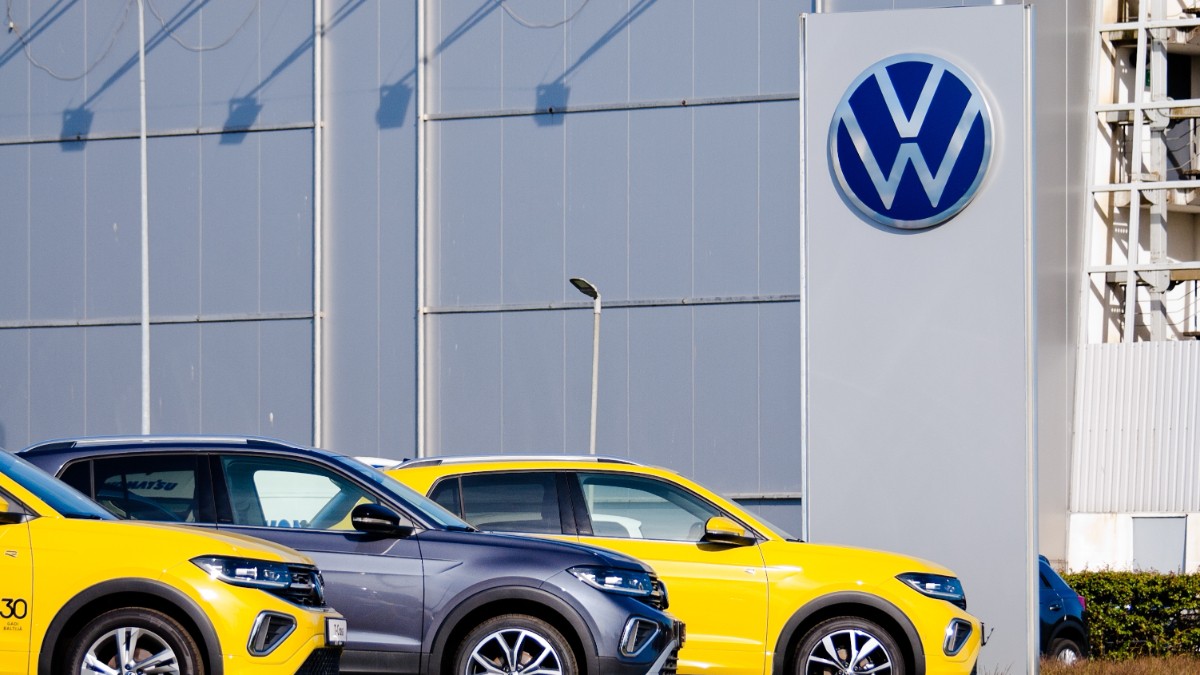 Mașini Volkswagen noi pe stradă, cu un zid gri în fundal.