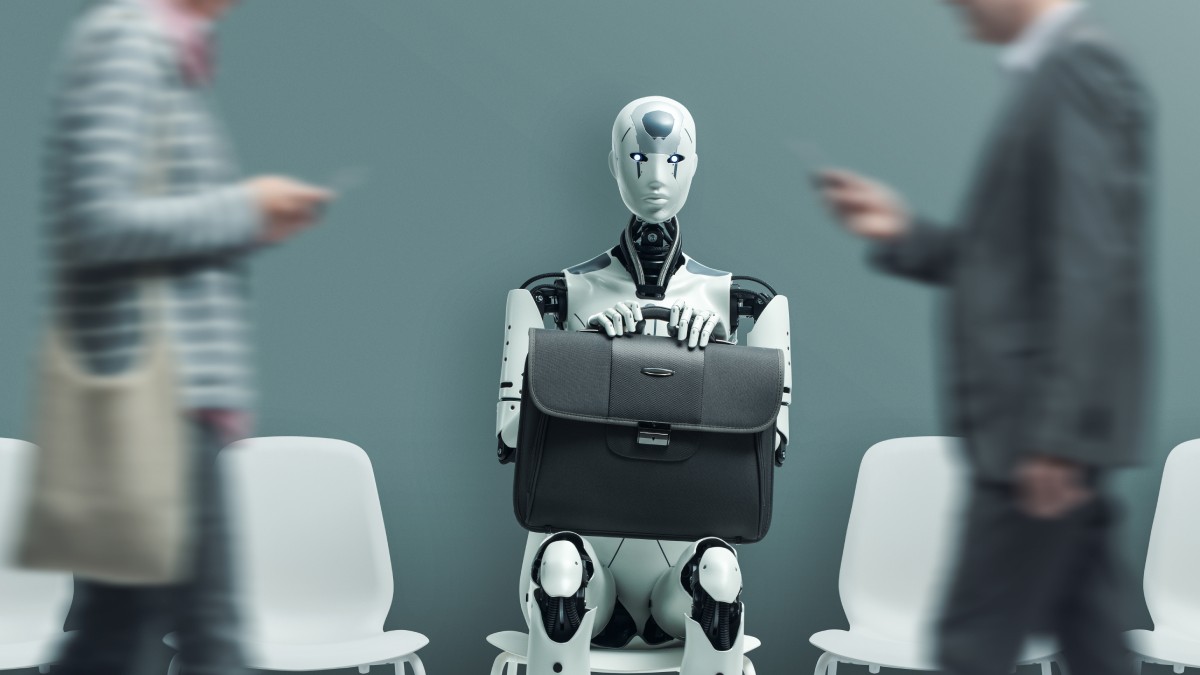 un robot cu o servietă neagră de muncă în brațe, stând pe scaun. pe lângă el trec doi oameni, cel din stânga este îmbrăcat cu o bluză cu dungi și are o sacoșă pe umăr, cel din dreapta este îmbrăcat într-un costum negru și are un telefon în mână
