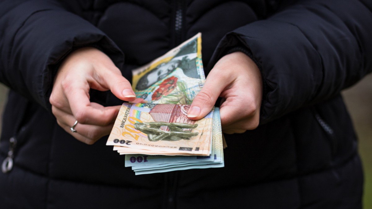 O femeie îmbrăcat în doliu cu o jachetă neagră, în timp ce numără un teanc de bani din ajutorul de înmormântare