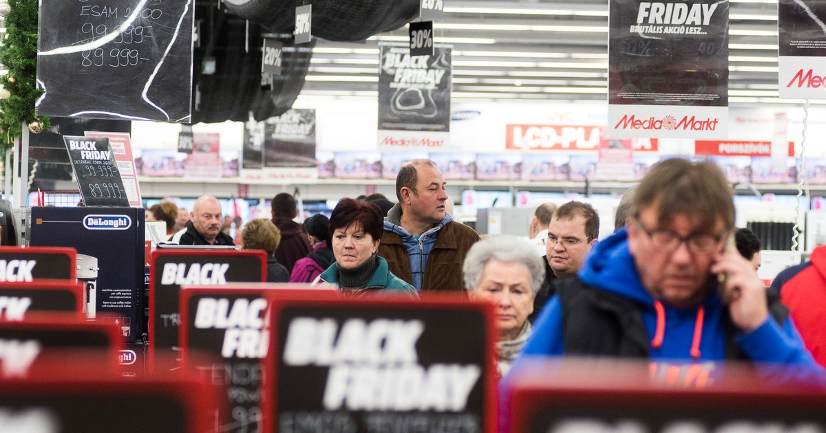 Altex, Media Galaxy și evoMag dau startul reducerilor de Black Friday începând cu 1 noiembrie. Oameni la coadă cu semne de reduceri de Black Friday pe lângă ei