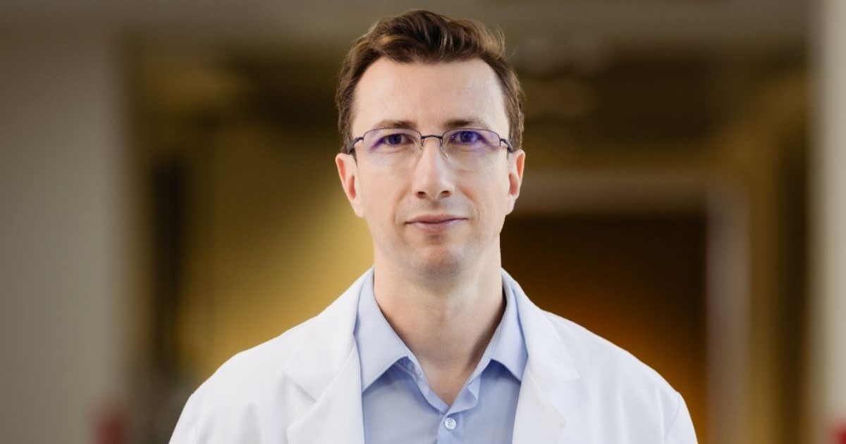 Dr. Cătălin Bosoancă, îmbrăcat cu un halat alb și o cămașă albastră, cu ochelari de vedere, pe fundal blurat