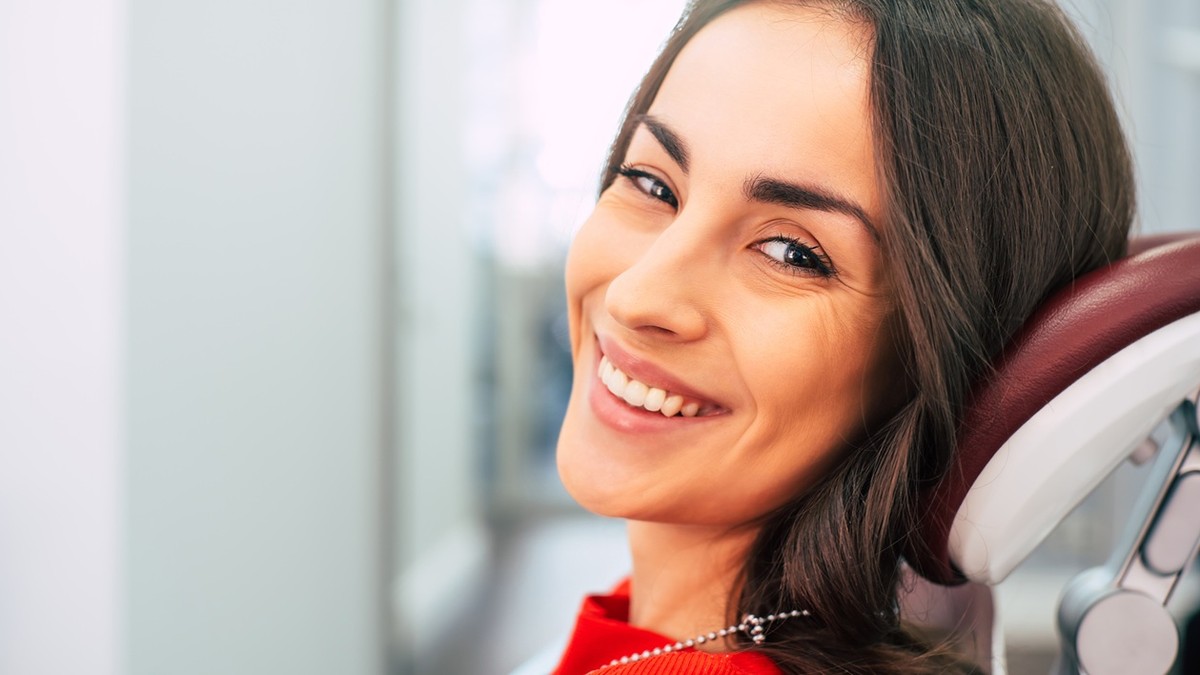 City Dental Clinic - femie satena asezata pe scaunul doctorului dentist, uitandu-se spre camera zambind