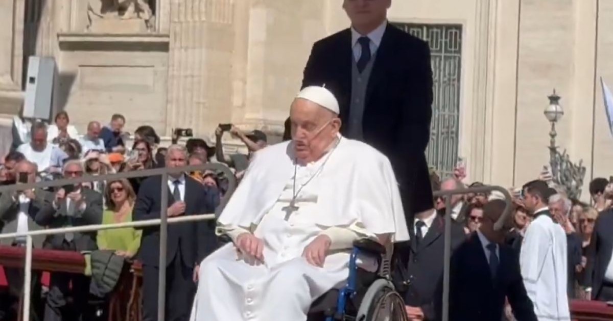 Papa Francisc in scaun cu rotile, impins de un bărbat, în multime