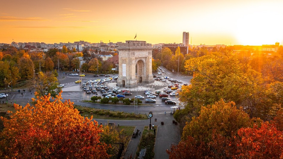 Fotografie aeriană care înfățișează Arcul de Triumf, un monument istoric din București, în timpul unui frumos apus de toamnă. 