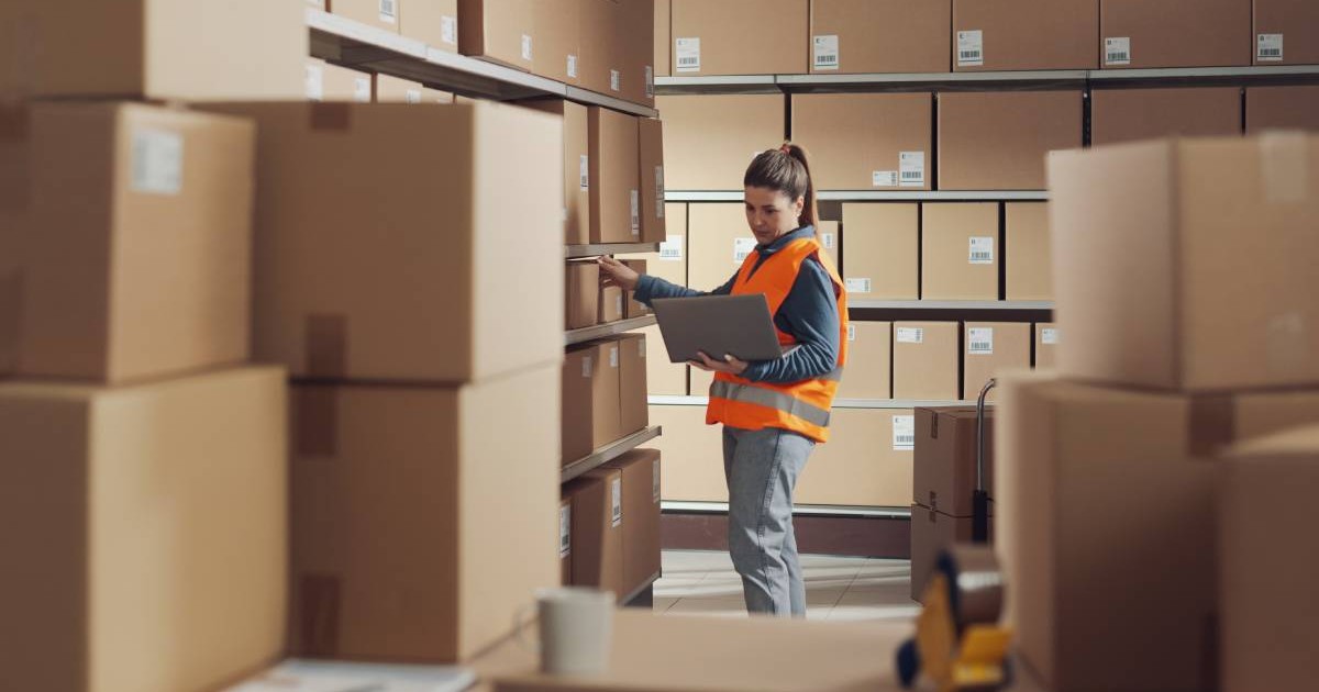 Femeie care lucrează cu un laptop la depozit, concept de logistică