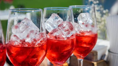 Se pune gheață în vin? Câteva pahare de vin umplute cu gheță și vin roze si puse pe un bar la o petrecere în aer liber