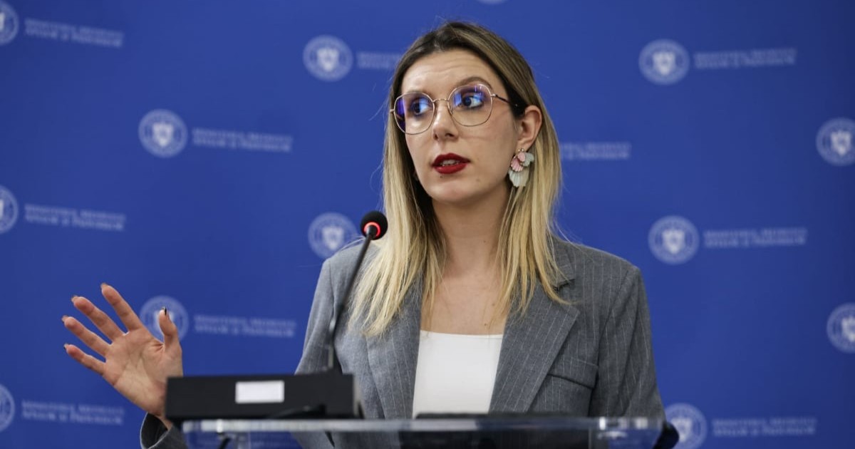 Diana Buzoianu într-un sacou gri și tricou alb în timp ce vorbește la microfon.