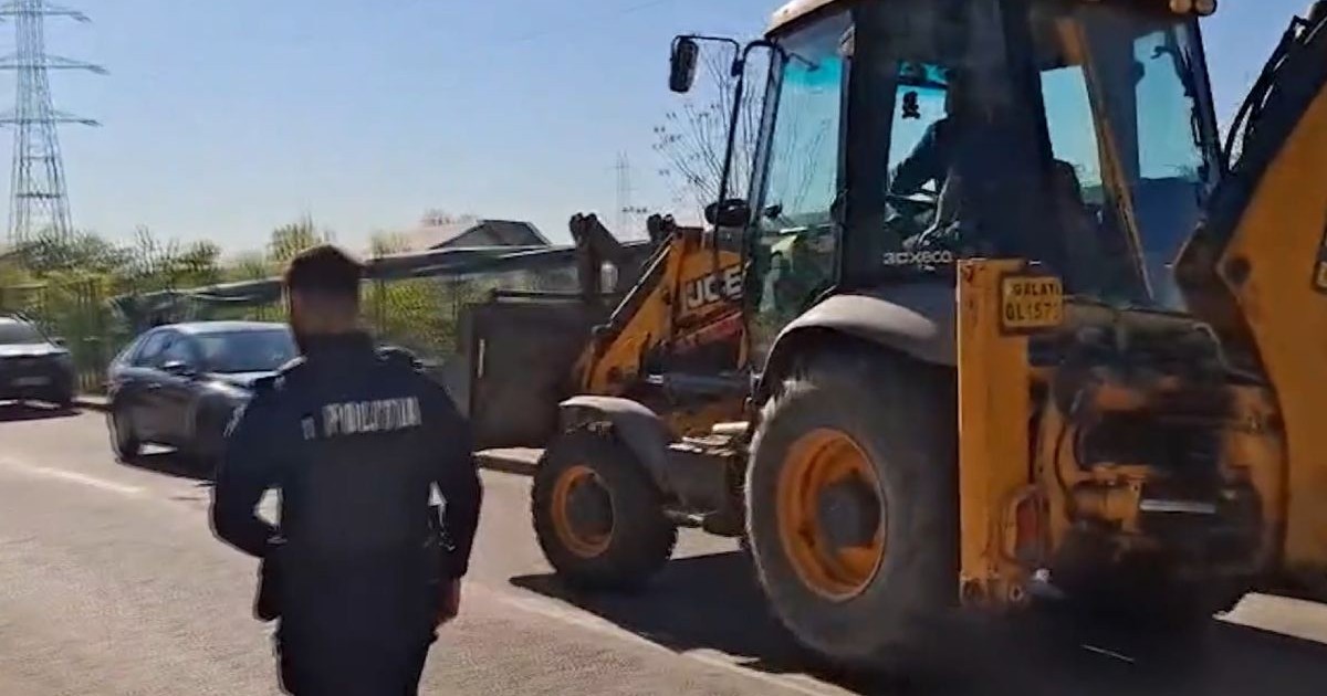 Buldoexcavator de culoare galbenă, cu cupă, tras pe dreapta de un polițist îmbrăcat în uniformă neagră, pe o stradă din Galați, pe 25 aprilie 2026