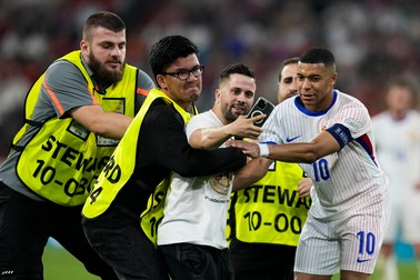 Kylian Mbappe of France, right, helps stewards remove a spectator from the pitch during a semifinal match between Spain and France at the Euro 2024 soccer tournament in Munich, Germany, Tuesday, July 9, 2024.,Image: 888579220, License: Rights-managed, Restrictions: This content is intended for editorial use only. For other uses, additional clearances may be required., Model Release: no