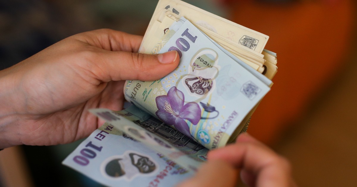 Un bărbat care numără bani și ține hârtii de 50 și 100 de lei în mână