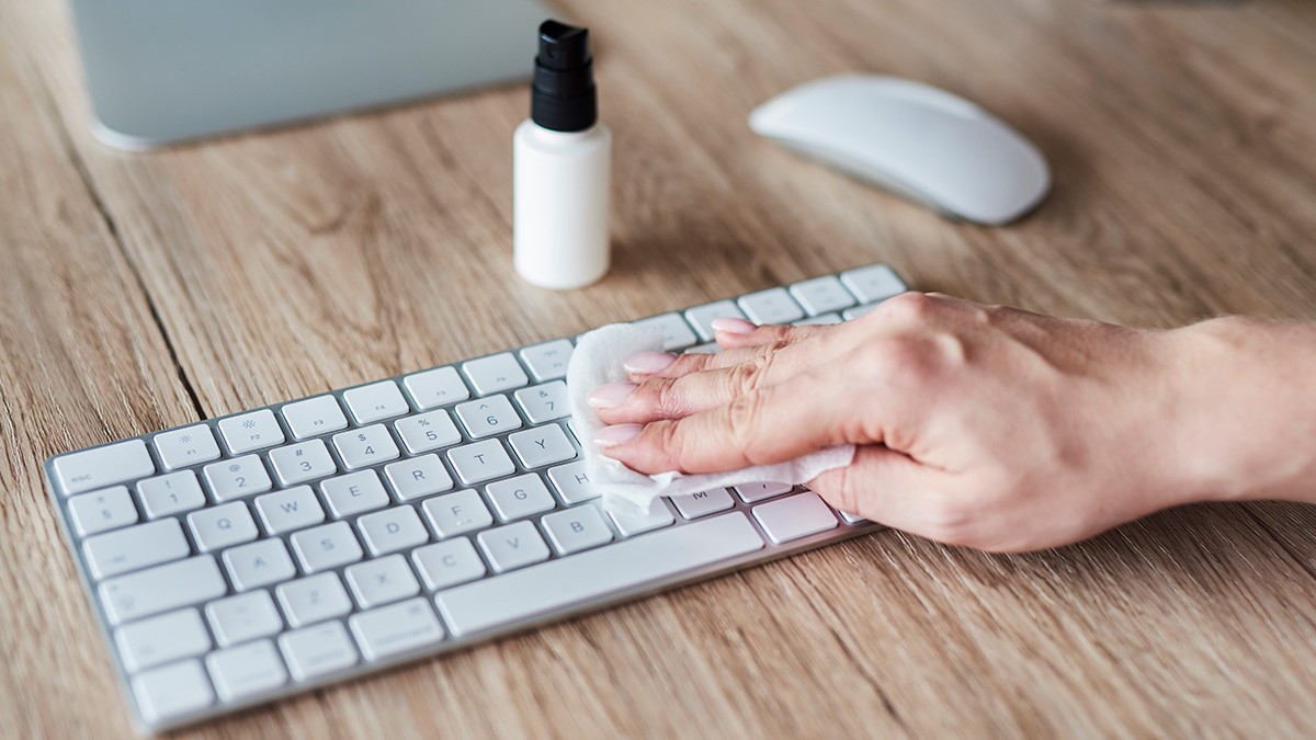 O mână curăță tastatura cu o soluție de dezinfectare.