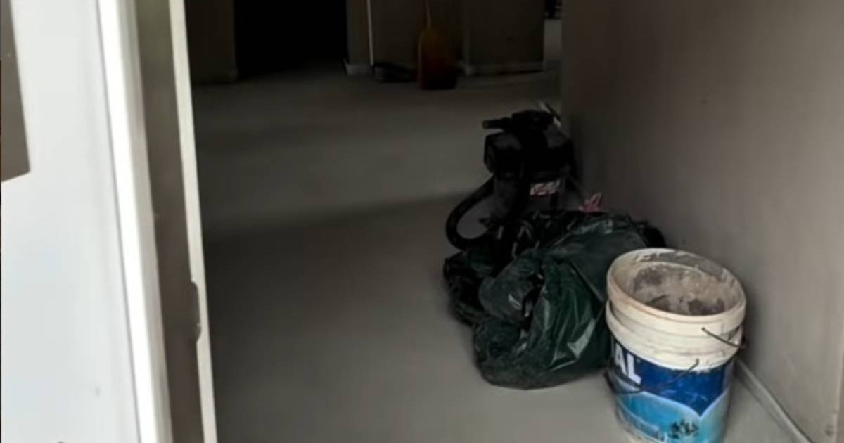Un hol lung, gol, într-o casă în renovare. Podeaua este finisată, dar pereții sunt simpli. Pe dreapta sunt găleți și saci de construcții, iar în spate se vede o zonă mai întunecată, semn că lucrările nu sunt încă gata.