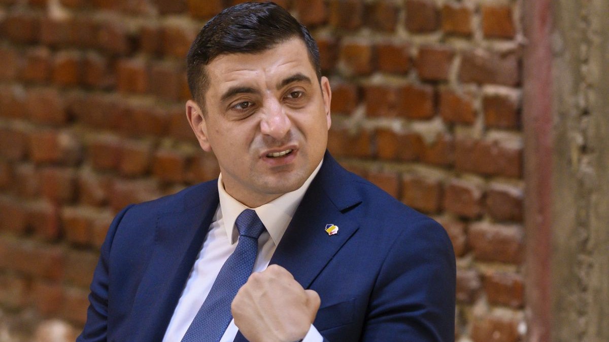 George Simion, îmbrăcat într-un costum de culoare albastră, având în spate un perete de cărămidă