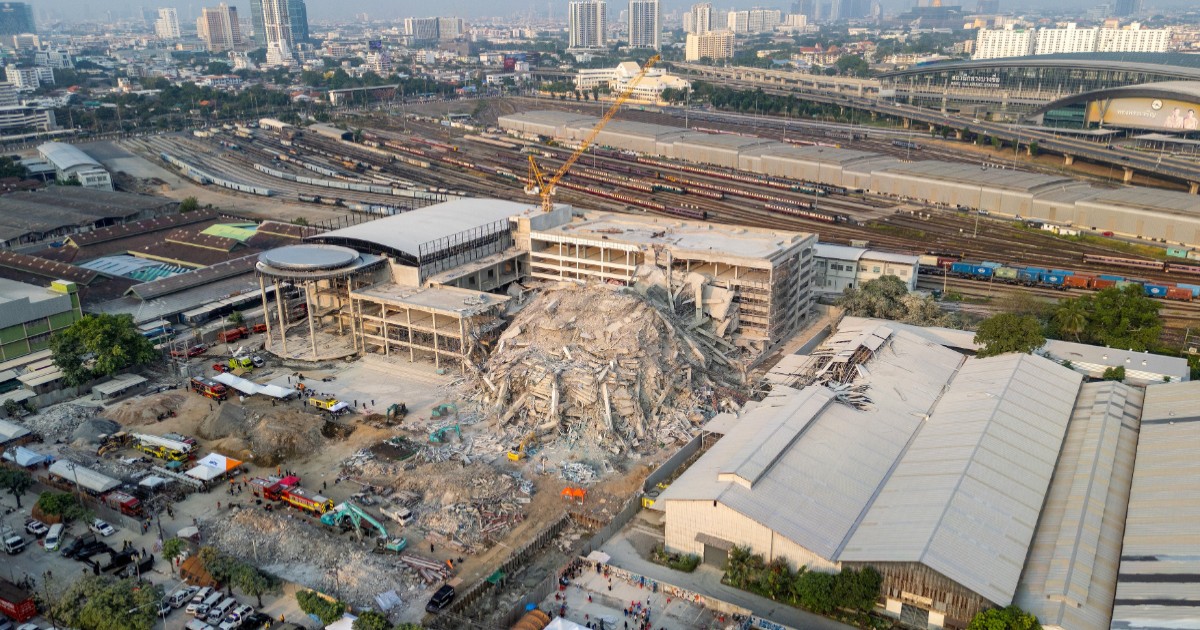Imaginea arată o clădire prăbușită din Bangkok. În fundal, există linii de cale ferată, clădiri înalte, mașini și oameni