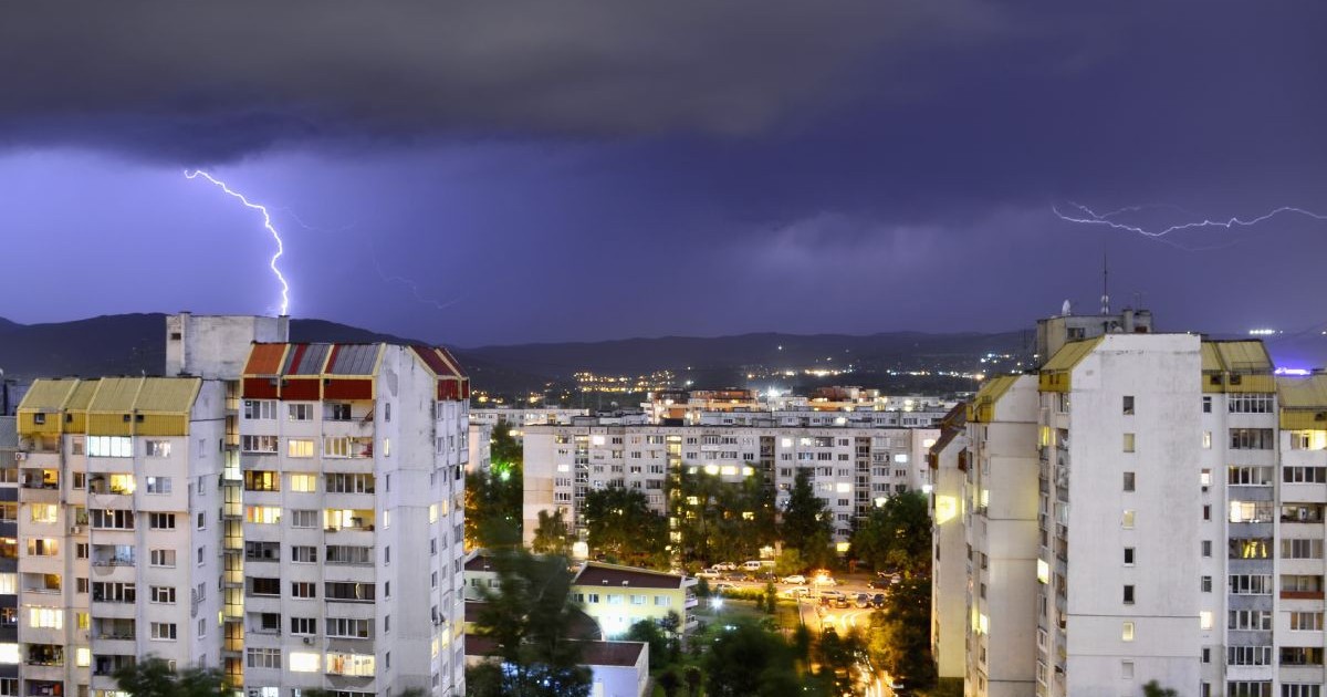 Furtună cu descărcări electrice pe fundal, iar în prim-plan mai multe blocuri dintr-un oraș