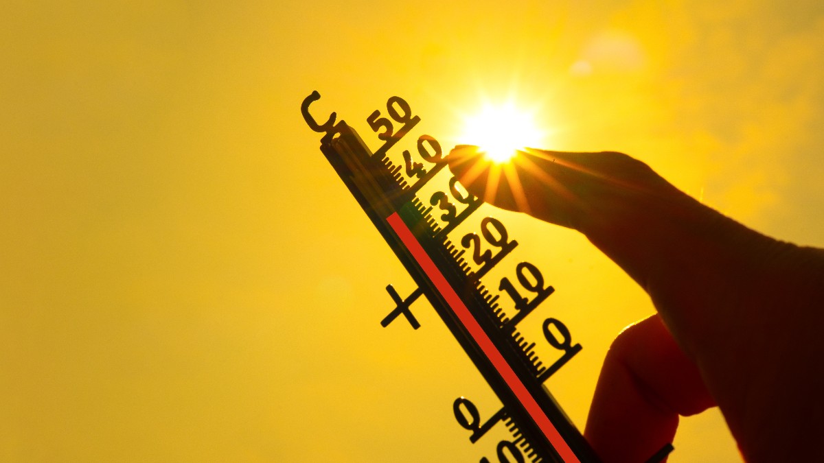 Imaginea prezintă o mână care ține un termometru orientat spre soarele puternic, indicând o temperatură ridicată de peste 35°C pe un fundal galben strălucitor.