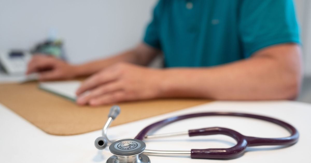 Un stetoscop stă pe un birou, lângă un doctor care consultă o fișă, 27 mai 2025